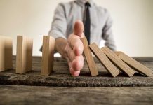 Hand stops falling dominoes on wooden table