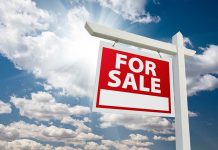 "For sale sign against cloudy sky backdrop."